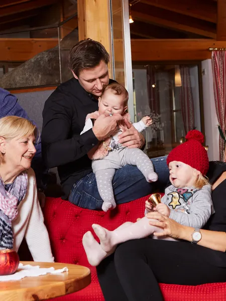 Das Suiten- und Generationenhotel Glöcknerin. Mehrgenerationenfamilie sitzt auf rotem Sofa in einem gemütlichen Wohnzimmer